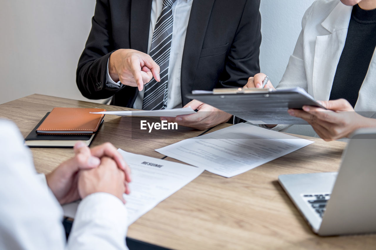 Midsection of business colleagues interviewing candidate by table at office