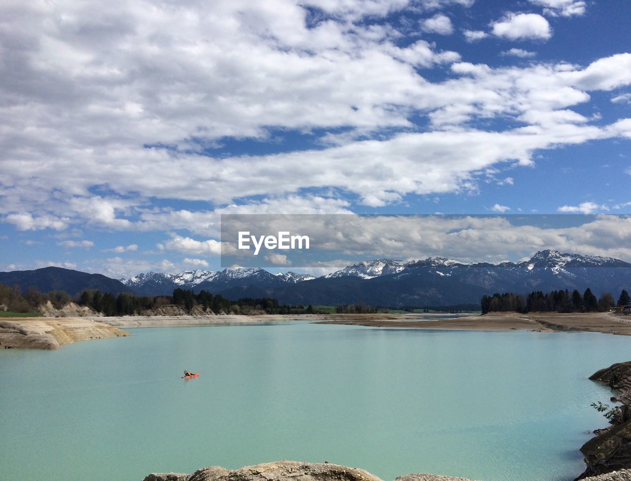 Scenic view of river and mountains against cloudy sky during sunny day