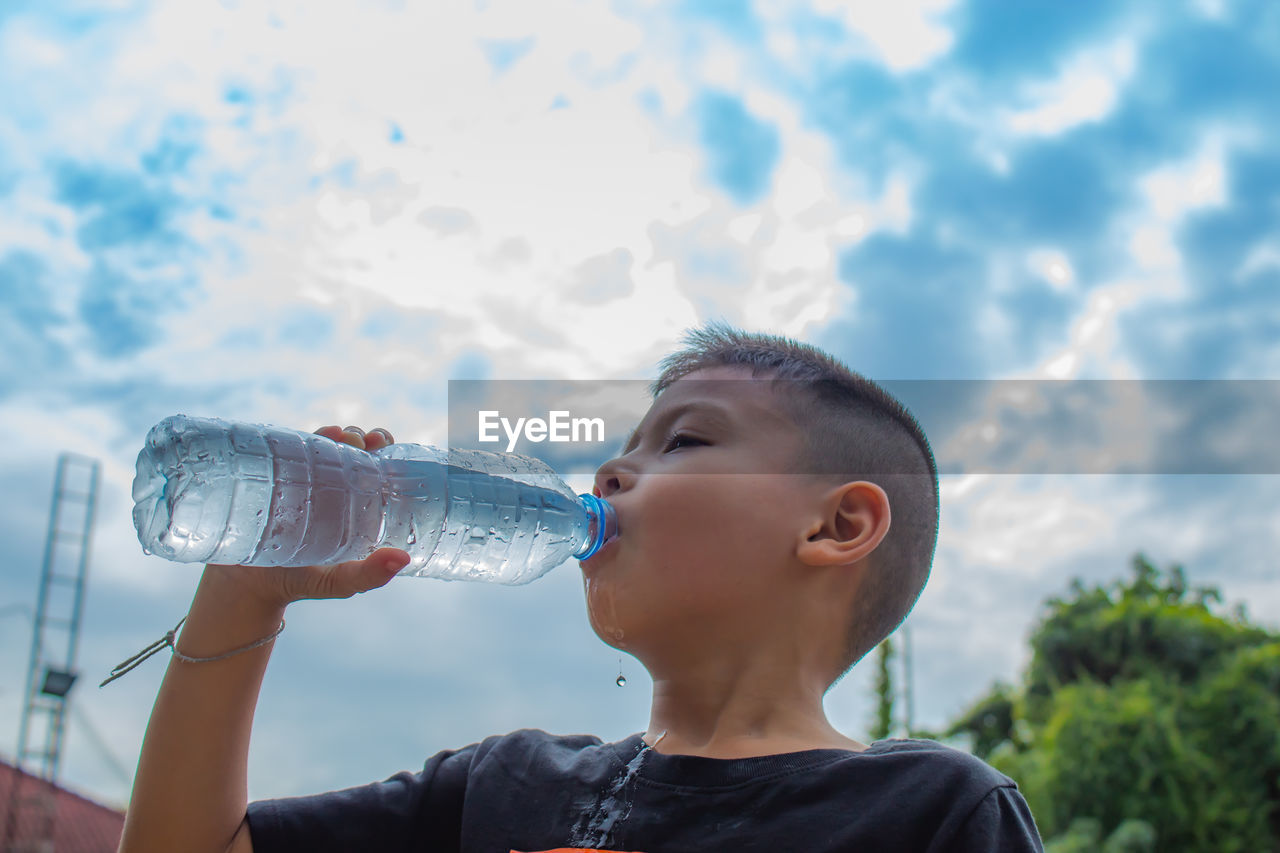 Boy drinking water from bottle against sky