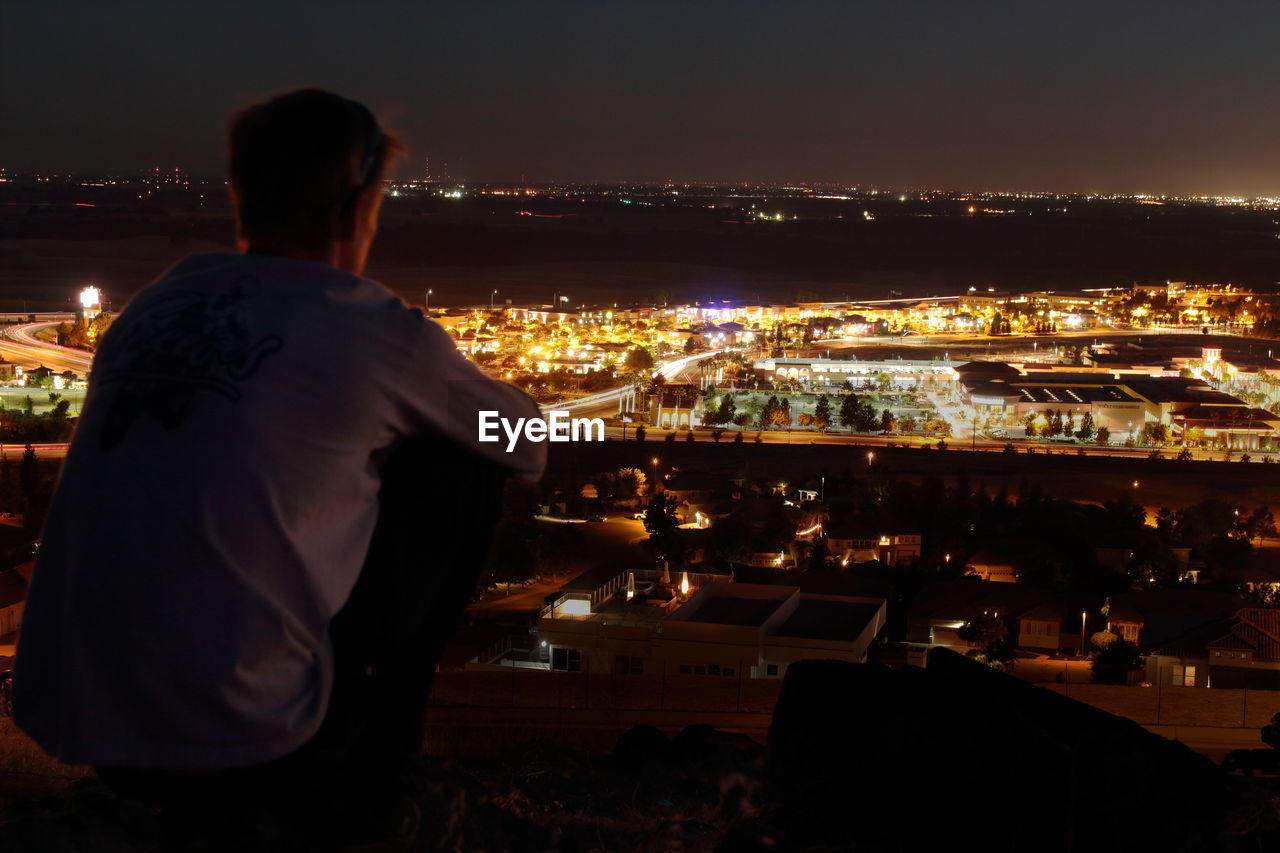 Rear view of man looking at illuminated city buildings in night