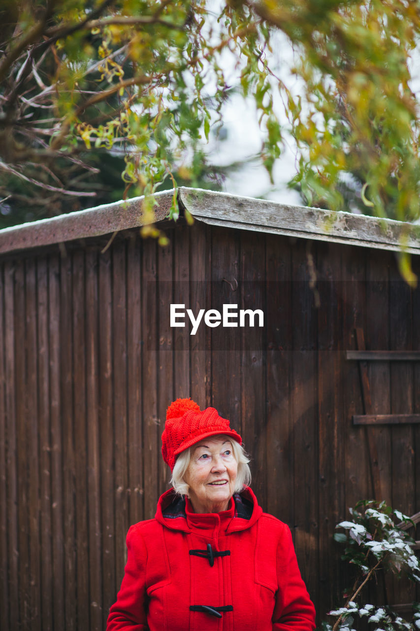 Portrait of senior woman standing against wooden house