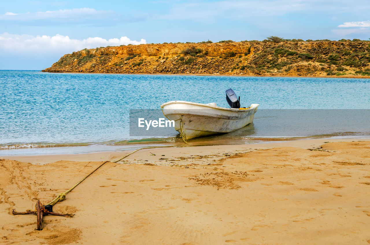 Boat anchored on shore at beach against sky