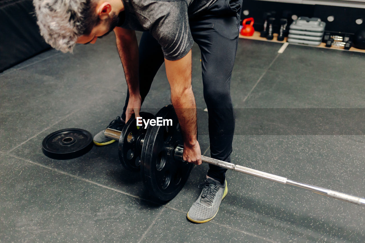 Male athlete in sportswear putting heavy plates on barbell while preparing for weightlifting workout in gym