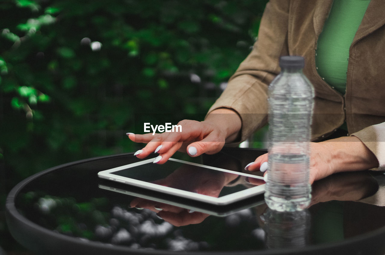 Hands of a young caucasian woman typing on the black screen of the tablet while sitting at a table