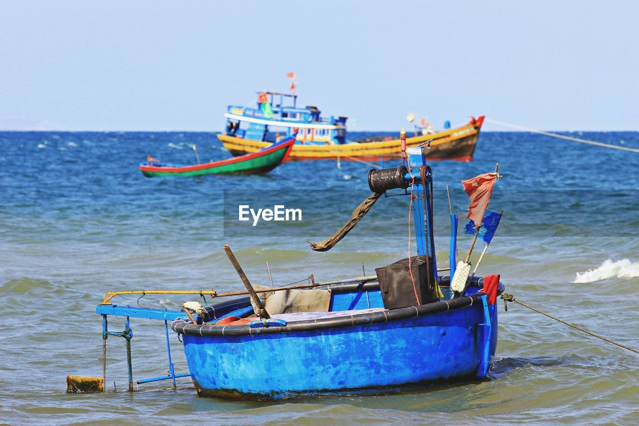 Fishing boats moored on sea against clear sky