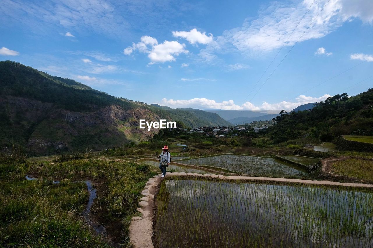 Woman walking in field against mountains and sky