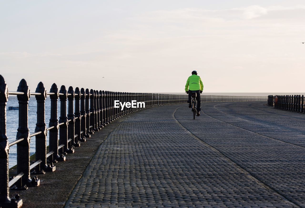 Rear view of man riding bicycle on bridge by sea against sky