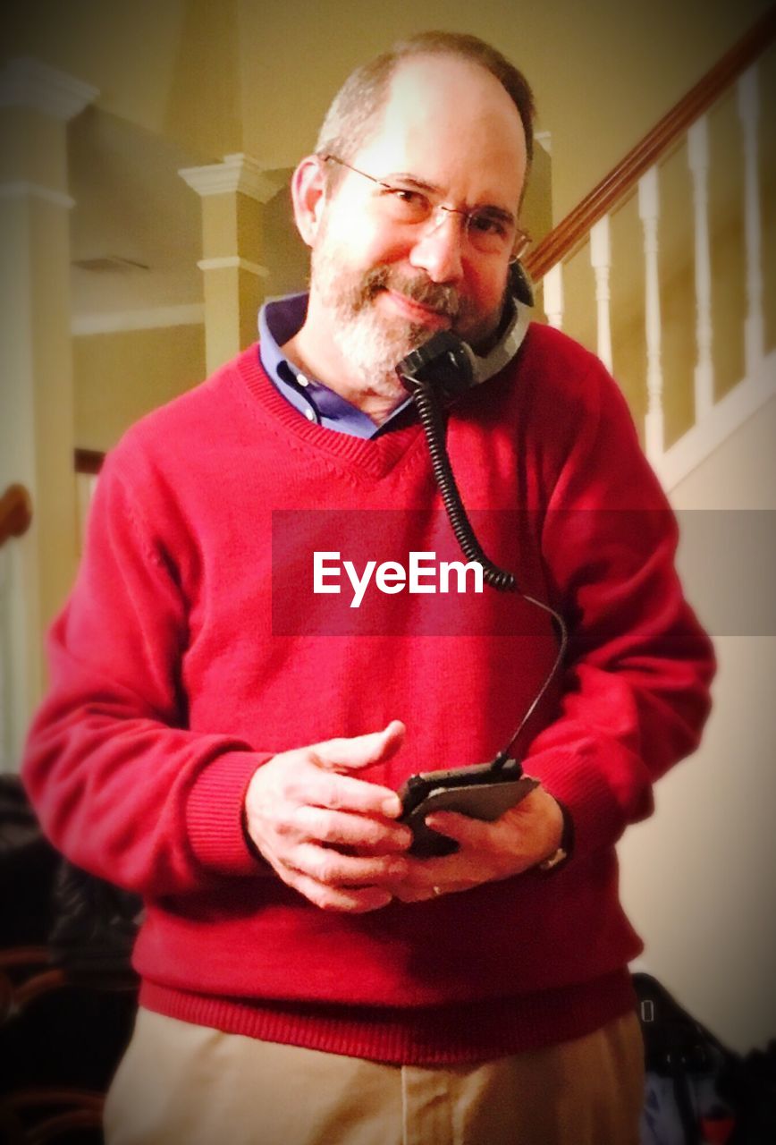 Portrait of mature man talking on telephone receiver plugged into smart phone at home
