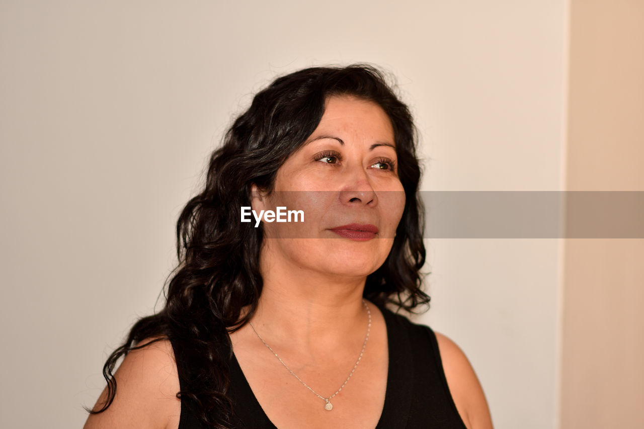 portrait, one person, adult, women, headshot, indoors, photo shoot, studio shot, hairstyle, looking at camera, female, front view, long hair, brown hair, person, copy space, portrait photography, human face, emotion, mature adult, looking, smiling, skin, black hair, black, serious, lifestyles, human hair, necklace