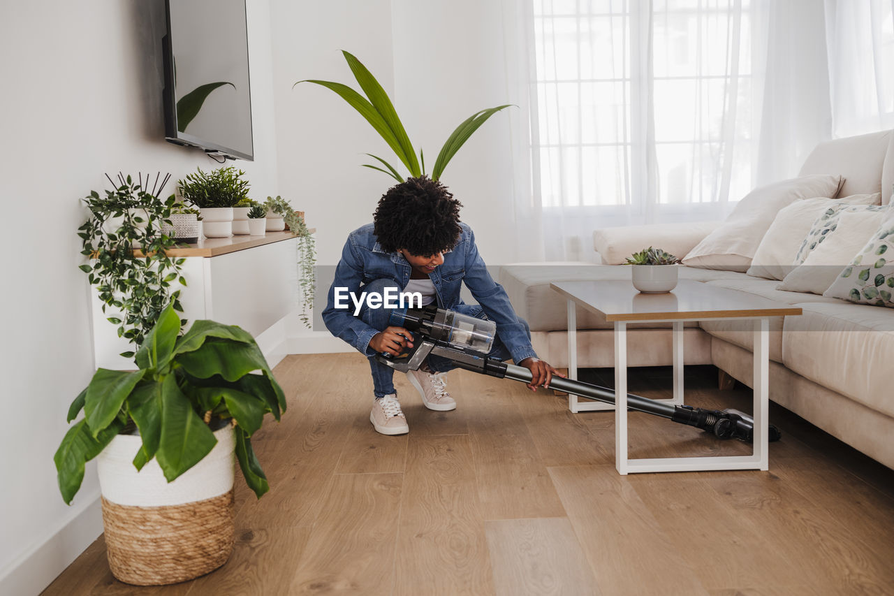 Young woman cleaning under coffee table in living room at home