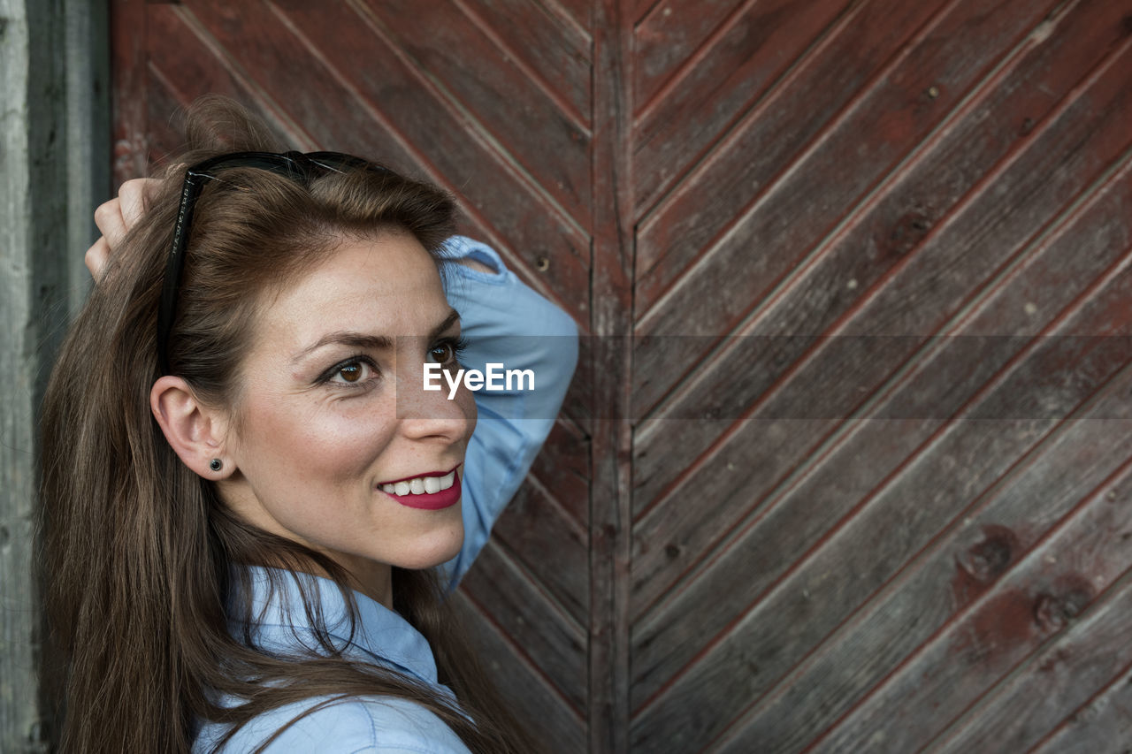 Close-up of smiling young woman by wooden door