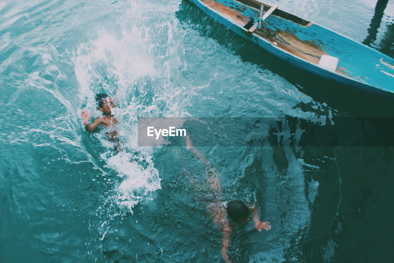 High angle view of boys swimming by boat on lake