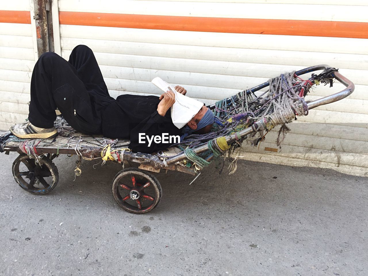 Man sleeping on cart against shutter at molavi square