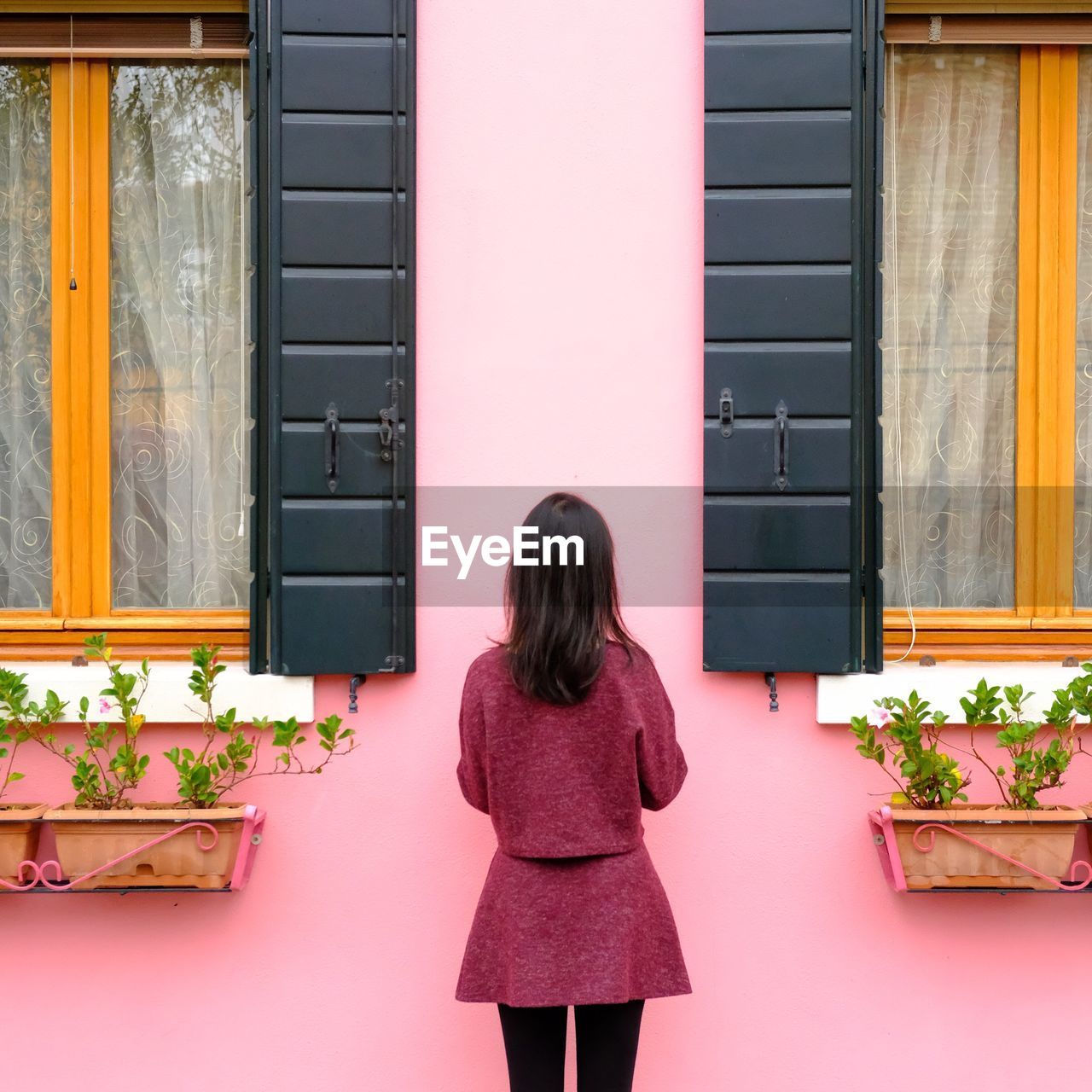 FULL LENGTH REAR VIEW OF WOMAN STANDING AGAINST WINDOW