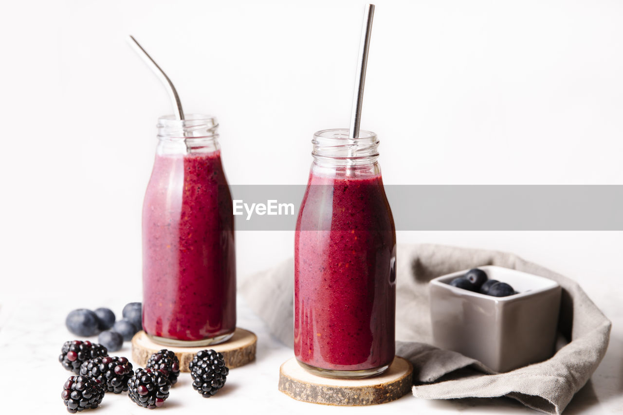 Berry smoothie in glass bottles with reusable metal straws. front shot with white background.