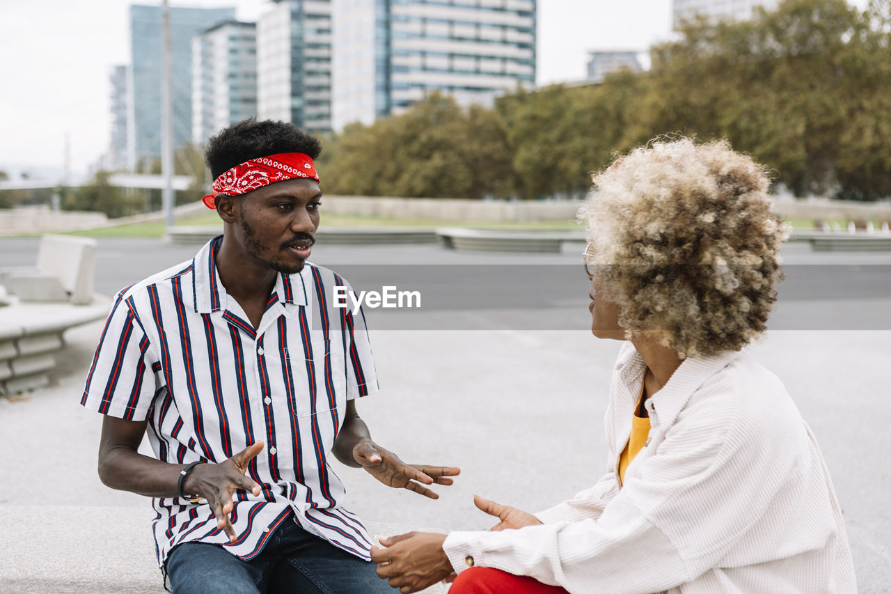 Mid adult friends talking while sitting on bench in city