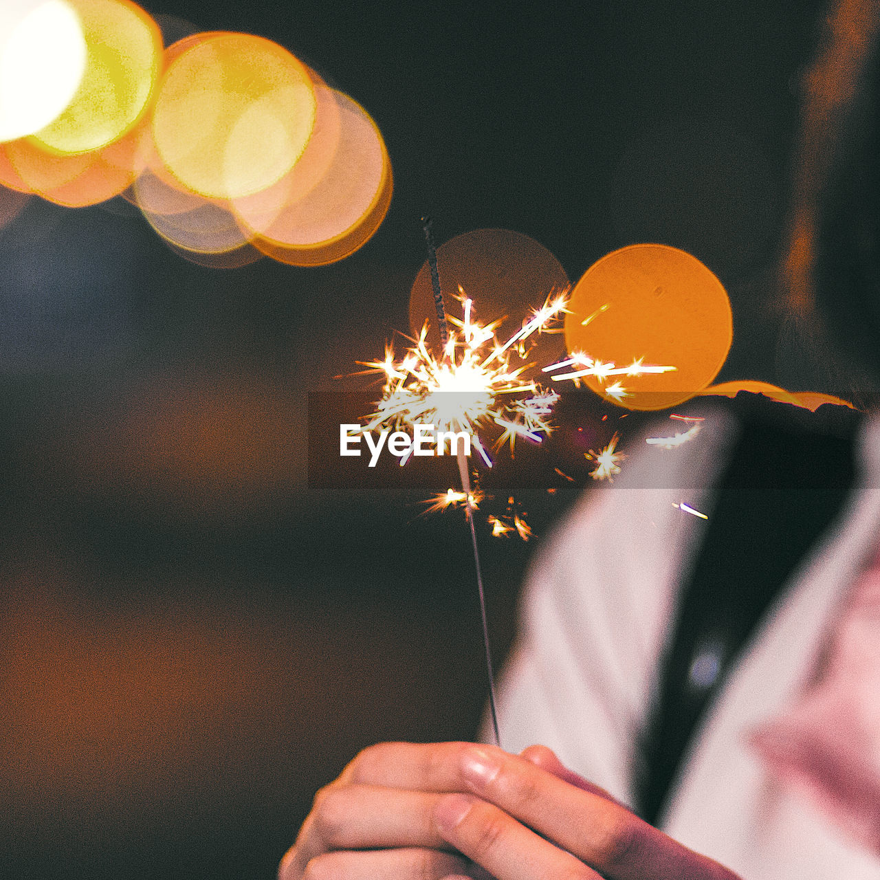 Close-up midsection of woman holding burning sparkler at night