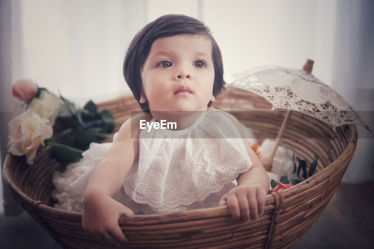 Close-up of cute baby girl looking away while sitting in wicker basket
