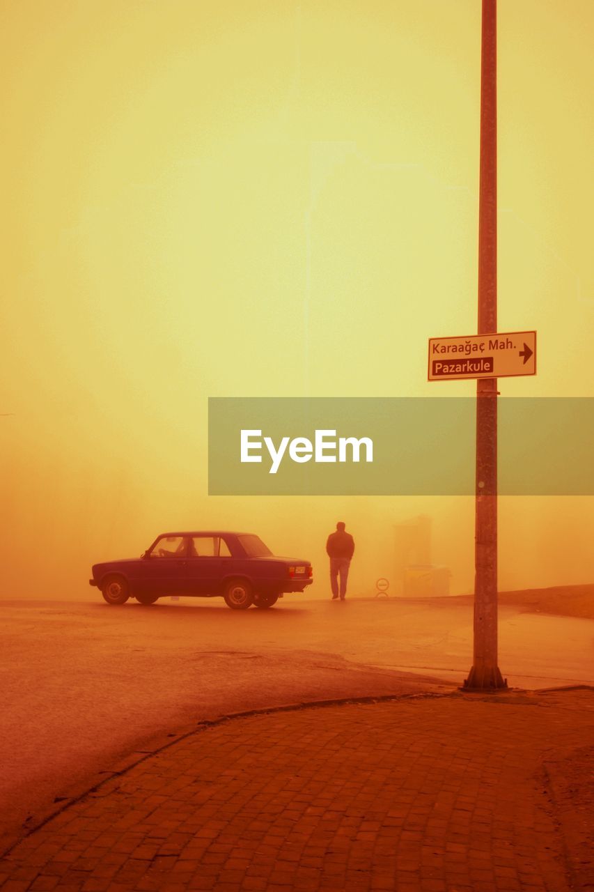 morning, sunrise, dawn, transportation, sky, mode of transportation, horizon, car, nature, orange color, motor vehicle, yellow, religion, sun, belief, desert, land, natural environment, land vehicle, sunlight, travel, vehicle, street, road, cross, spirituality, one person, outdoors, fog, beauty in nature, symbol