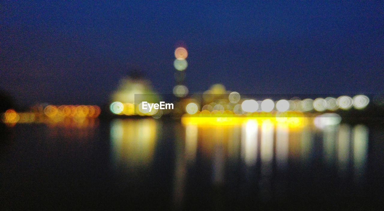 Defocused image of illuminated city by river at night