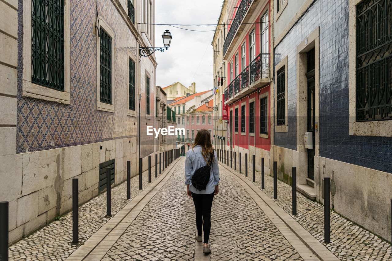 Woman walking on narrow alley amidst buildings