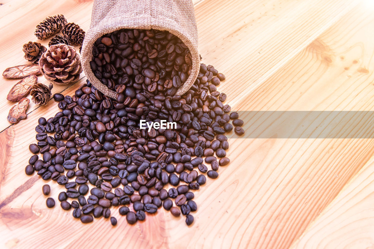High angle view of roasted coffee beans with pine cones on wooden table