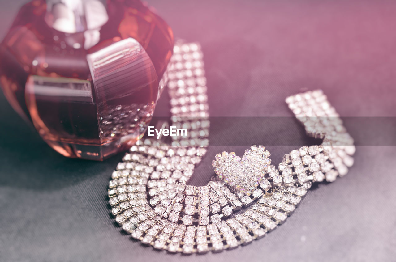 High angle view of diamond necklace and perfume on table