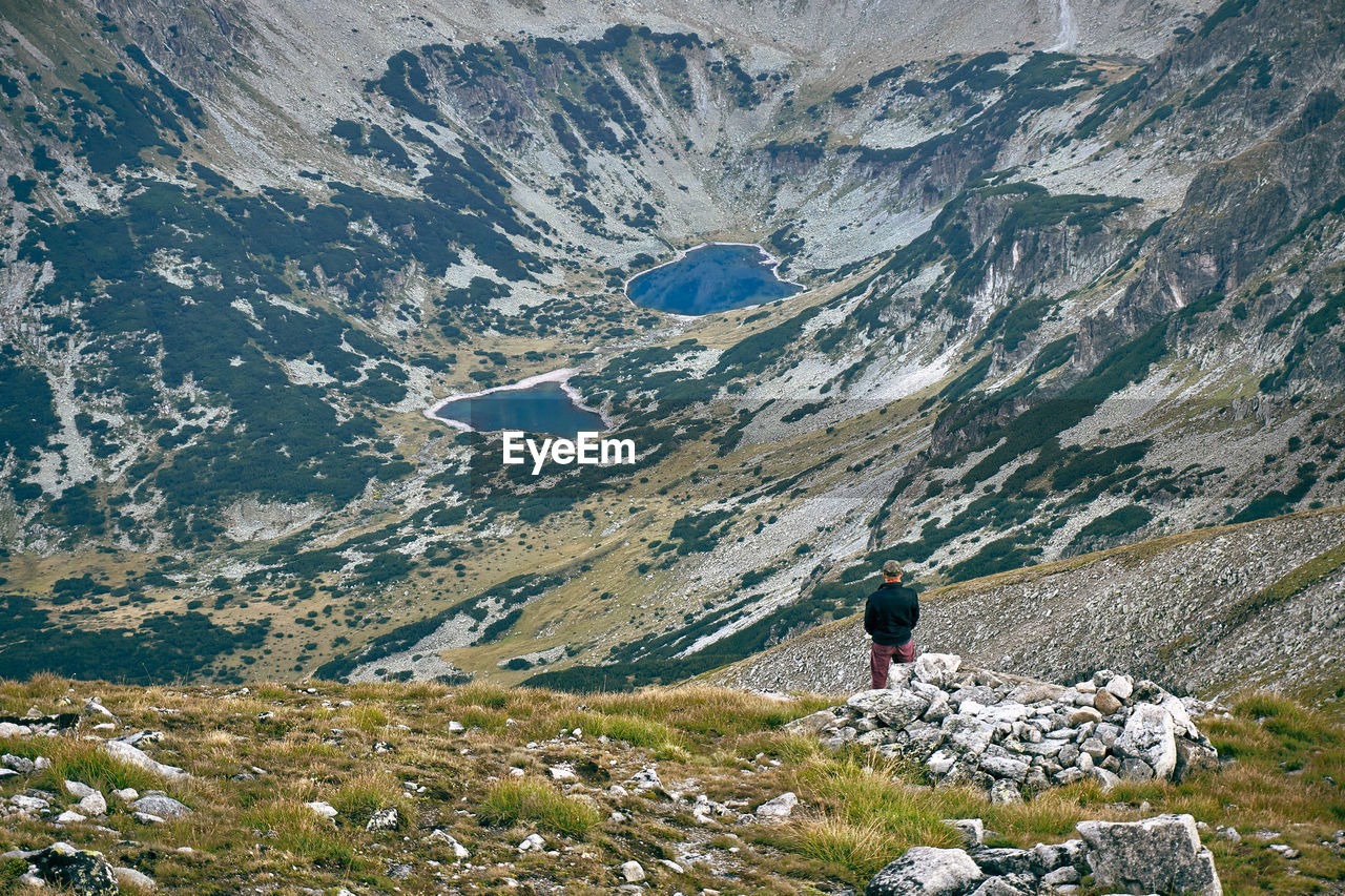 REAR VIEW OF PERSON ON ROCK AGAINST MOUNTAIN