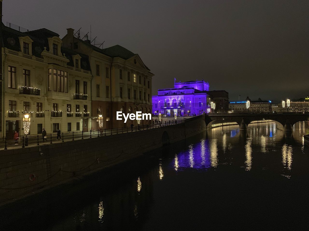 ILLUMINATED BUILDINGS BY RIVER IN CITY AT NIGHT