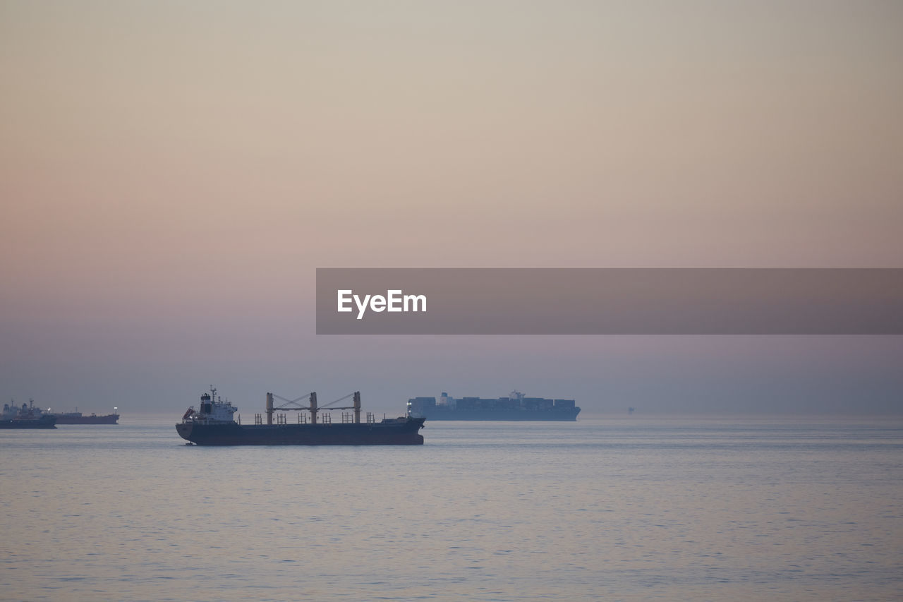 Commercial ships anchored at sea at sunset.