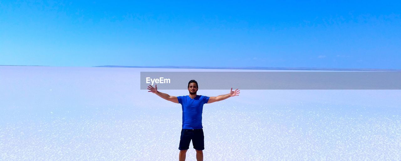 Young man standing on salt flat against clear blue sky