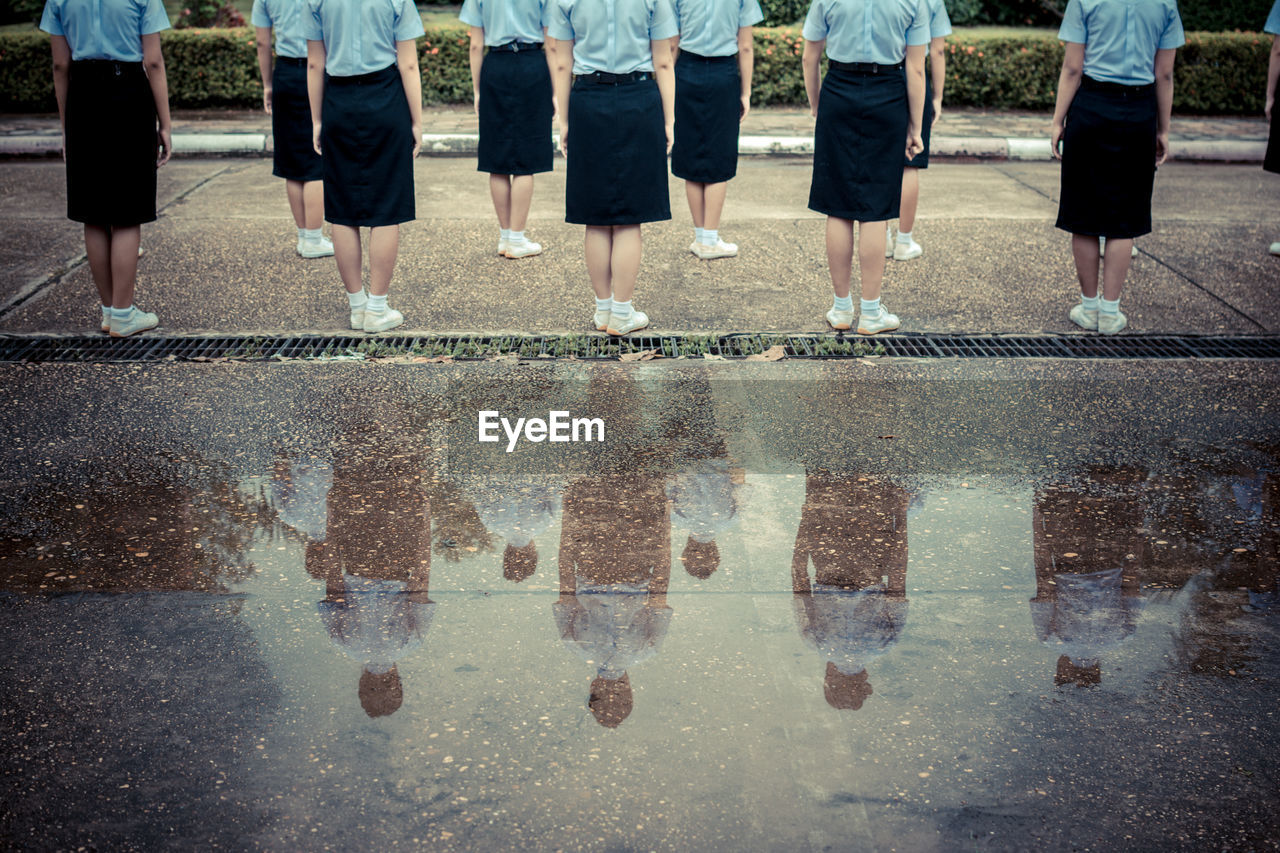 Low section rear view of women wearing uniform while standing on street by puddle