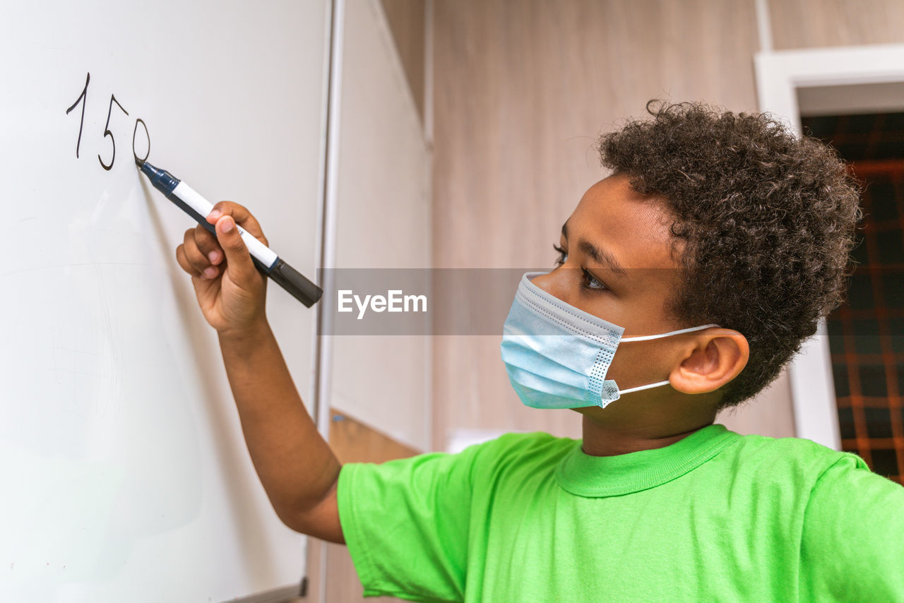 Close-up of boy wearing mask writing on whiteboard