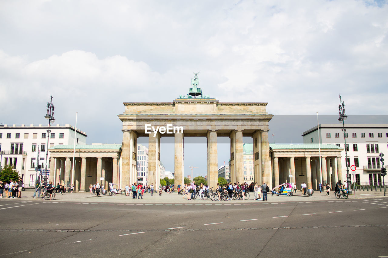 People in front of brandenburg gate against cloudy sky