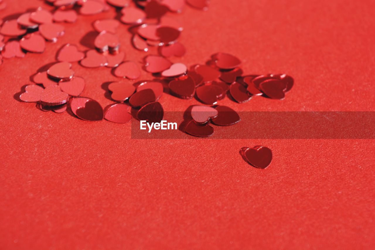 Heart shaped, red, shiny confetti on a red background with copy space
