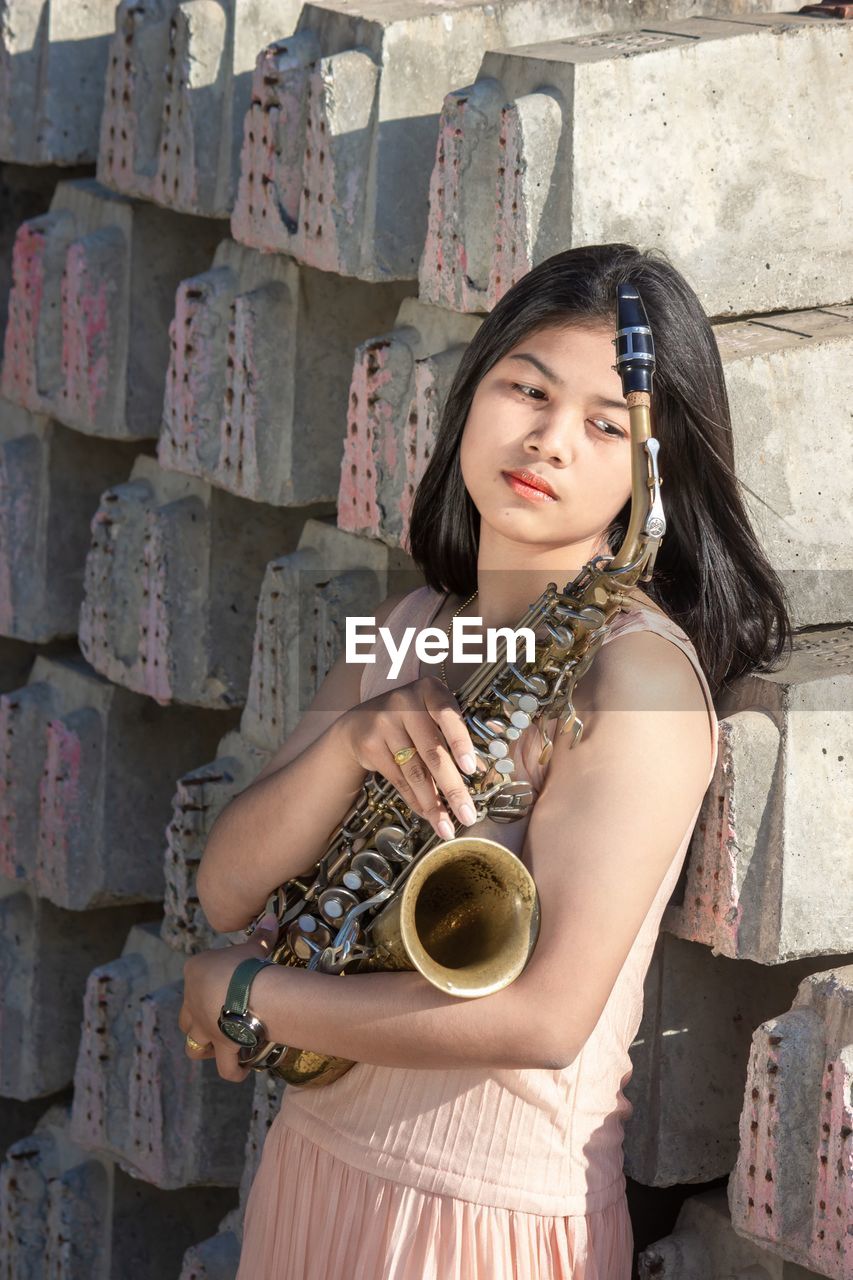 Portrait of a beautiful young woman standing against wall and holding saxophone with love emotional