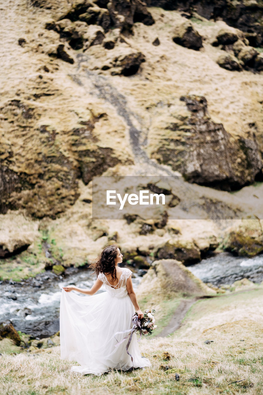 REAR VIEW OF WOMAN SITTING ON ROCK AT LAND