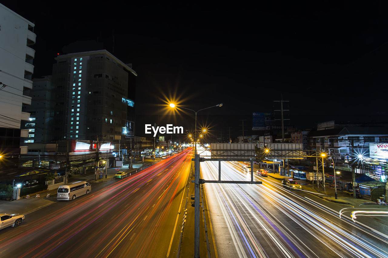 LIGHT TRAILS ON ROAD ALONG ILLUMINATED STREET LIGHTS AT NIGHT