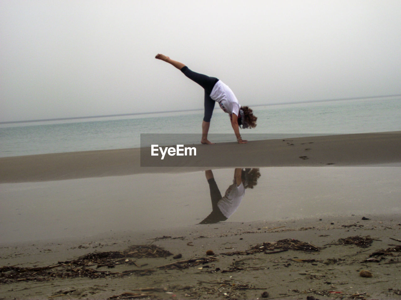 Full length of woman doing yoga on beach against sky