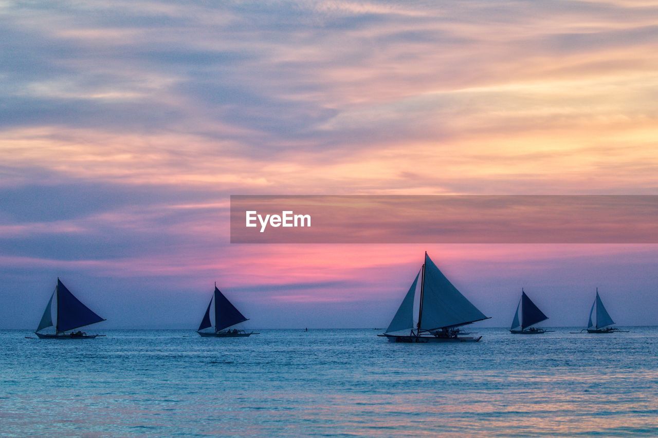 Sailboats sailing in sea against sky during sunset