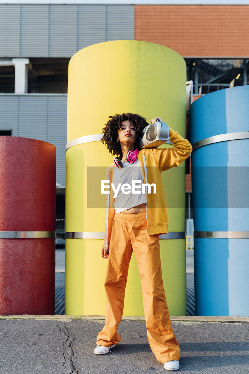 Young woman carrying boom box on shoulder in front of colorful pipes