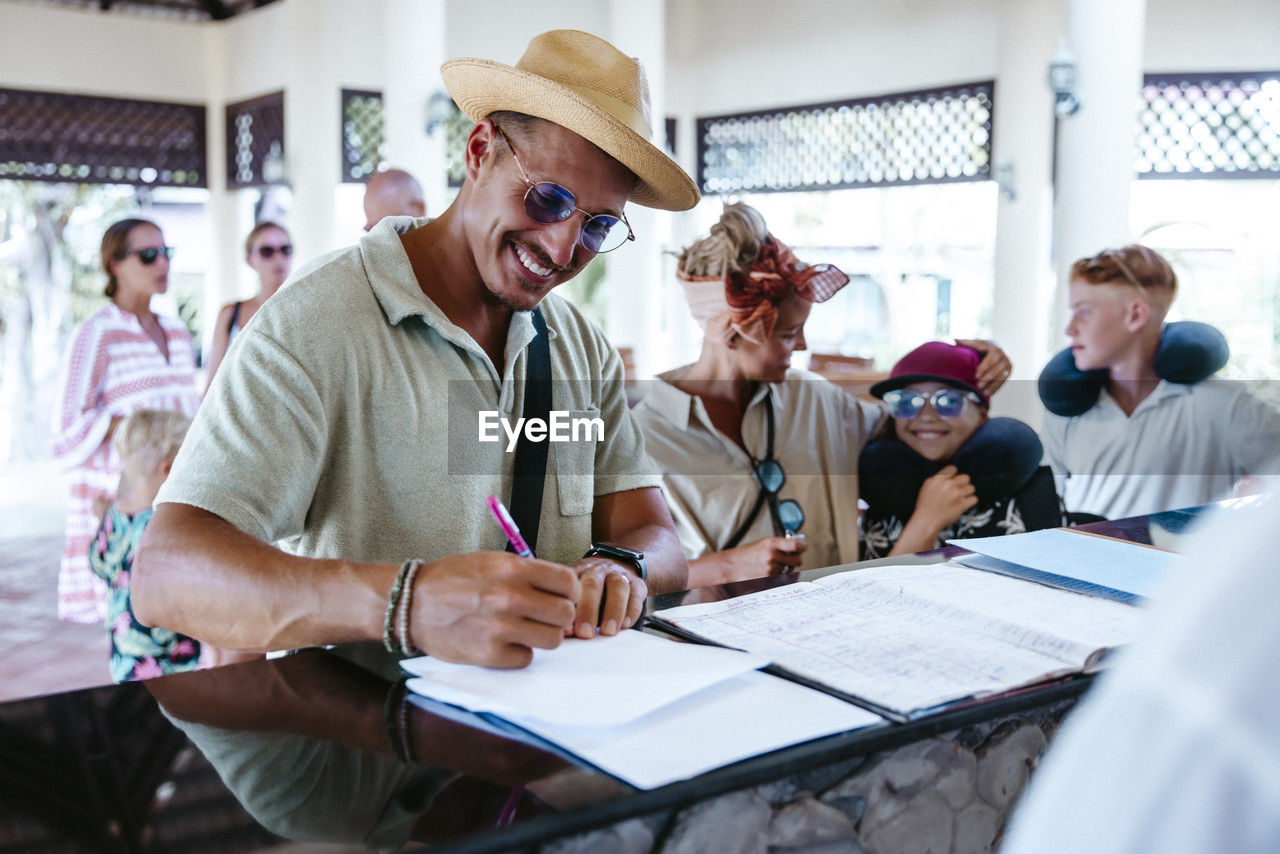 Happy man filling form at resort reception desk during vacation