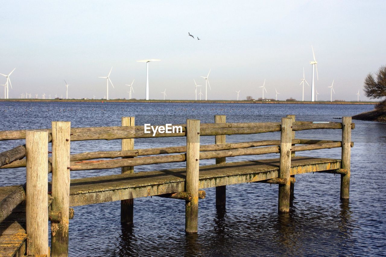 Wooden pier on lake with wind turbines in background