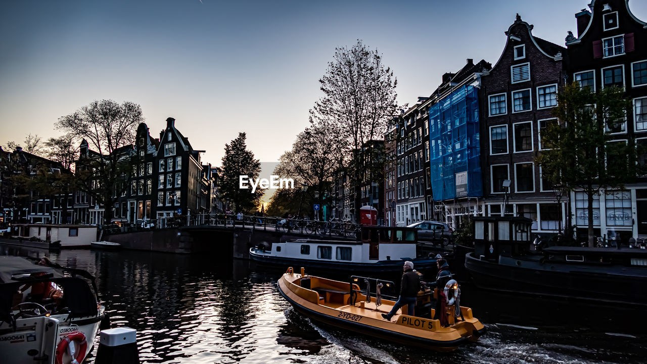 BOATS IN CANAL AMIDST BUILDINGS IN CITY