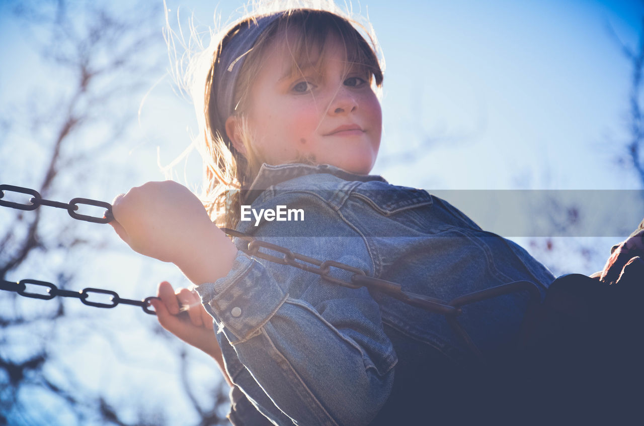 Side view portrait of cute girl swinging at playground during sunny day