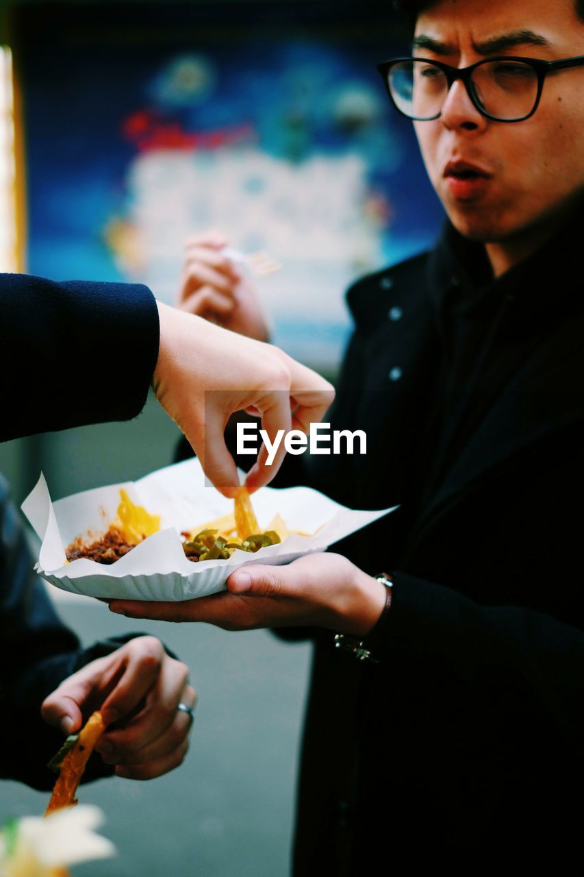 Cropped hand of man having french fries from plate held by friend