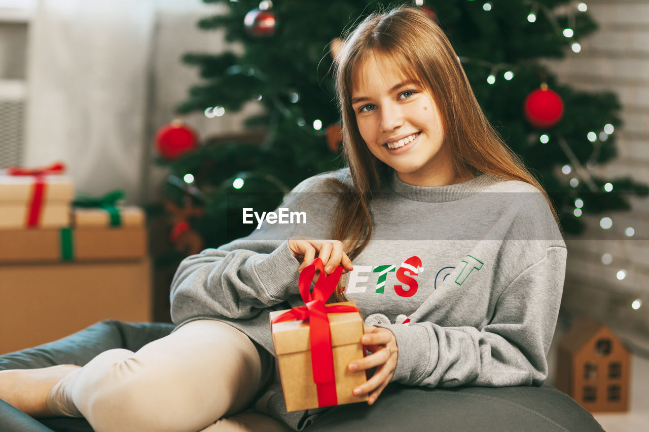 Beautiful teenage girl opens a gift made of kraft paper tied with a red ribbon