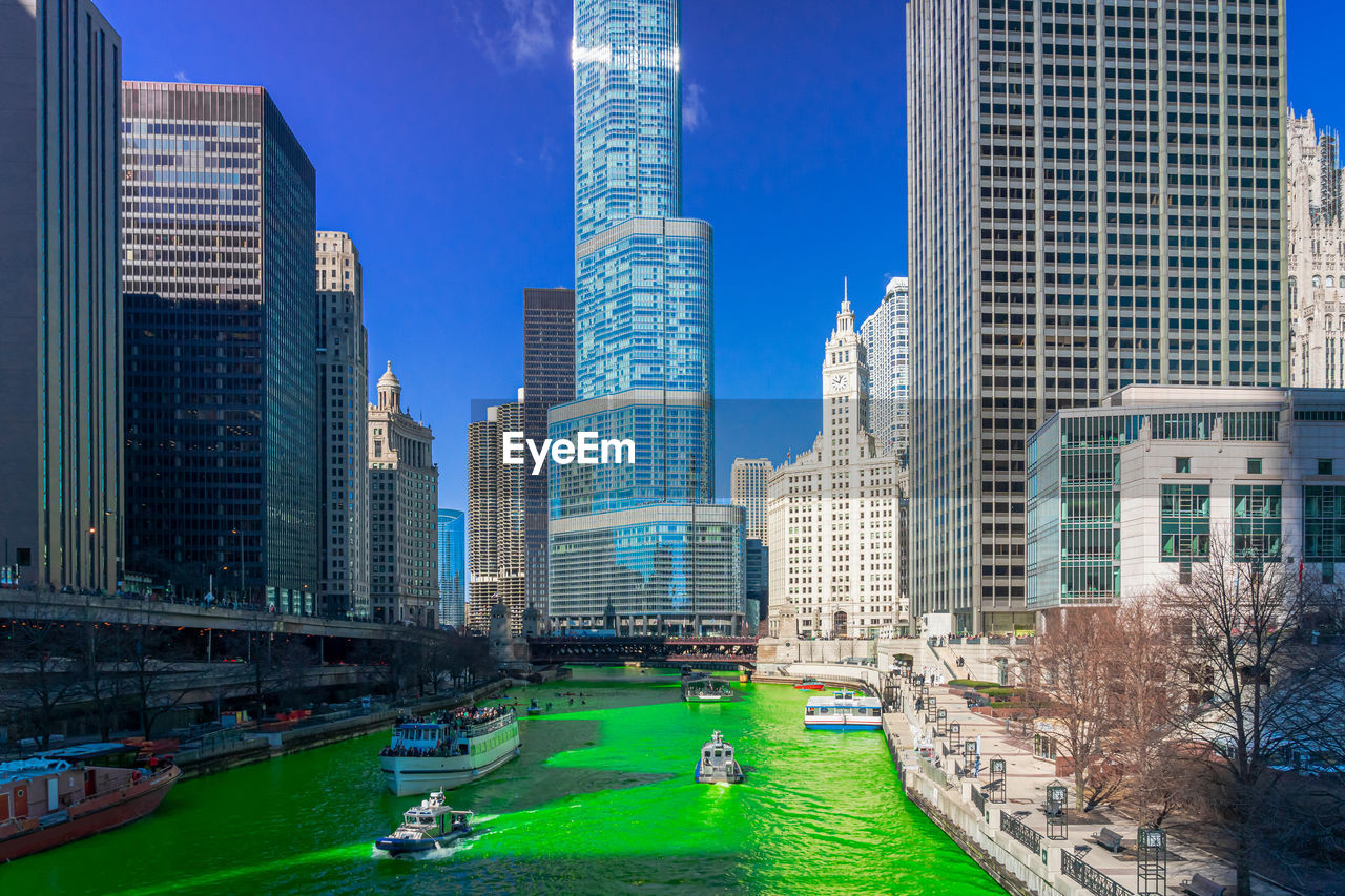 Modern buildings by canal in city against sky