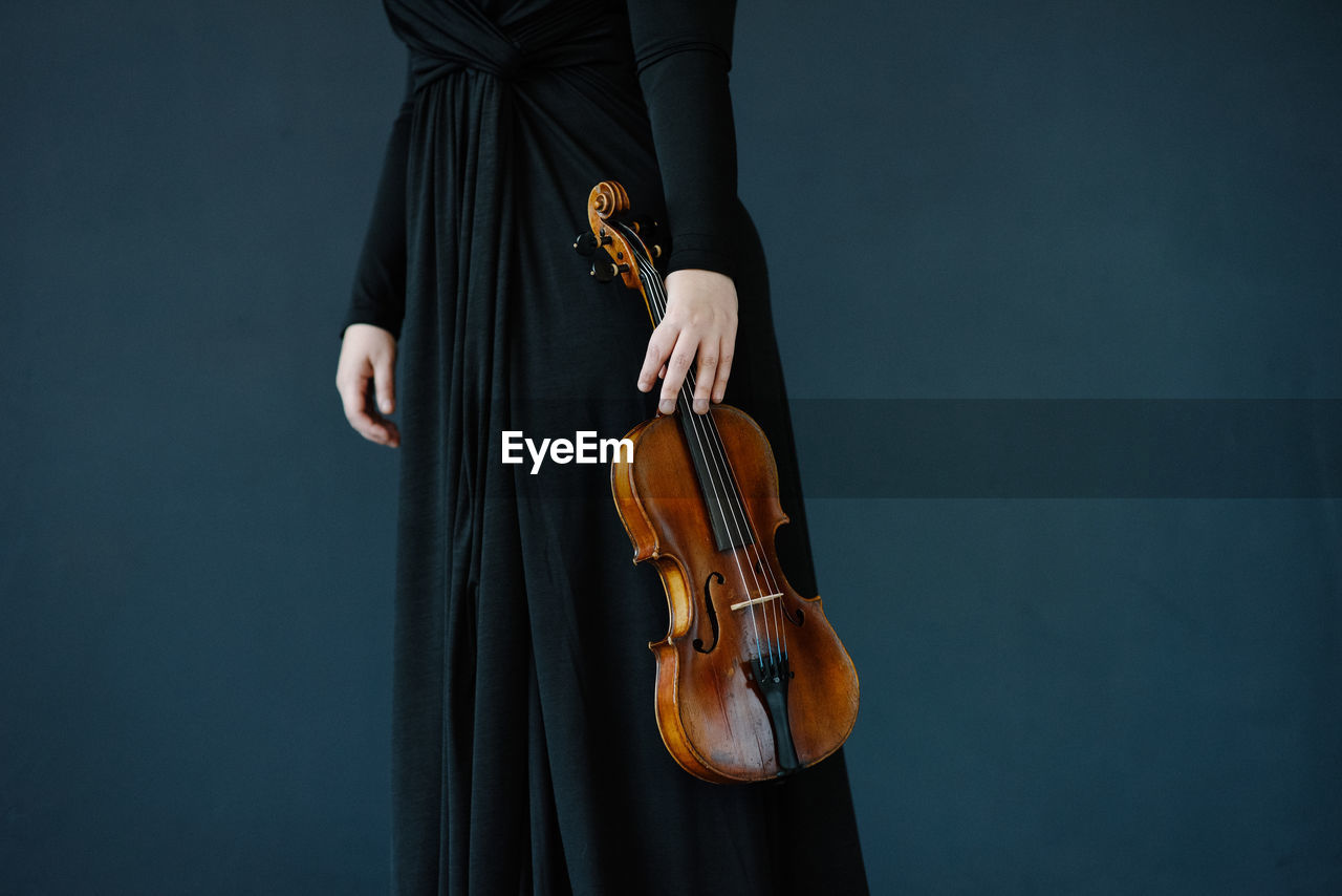 Midsection of woman holding violin against blue background