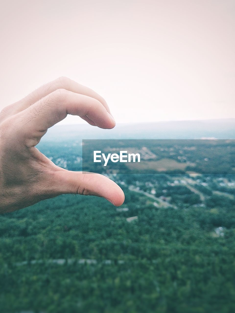 CLOSE-UP OF HAND ON LANDSCAPE AGAINST SKY